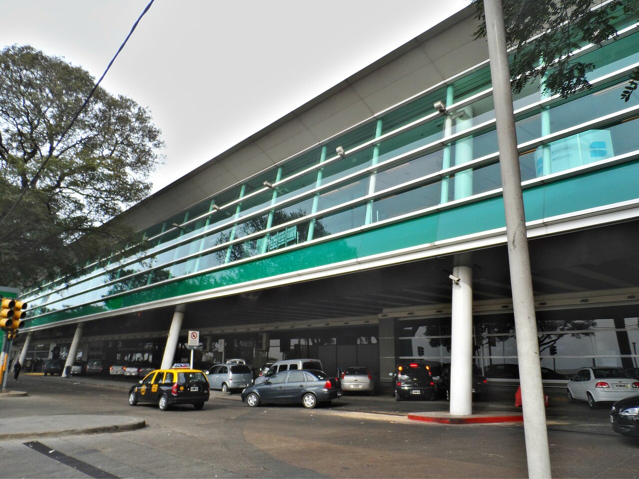 Fachada de la terminal del Aeroparque Jorge Newbery con autos y un taxi en la calle
